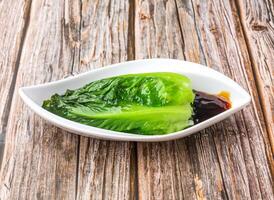 lettuce leaf with soy sauce served in dish isolated on wooden table side view of hong kong food photo