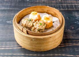 Pork and Shrimp Siomai served in bamboo steamer isolated on wooden table side view of hong kong food photo