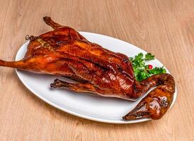 Roasted Goose Whole with coriander served in tray dish isolated on wooden table side view of hong kong food photo