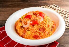 Western fried rice including shrimp and tomato served in plate isolated on napkin side view of hong kong food on wooden background photo