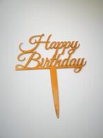 Gold Happy Birthday Cake Topper perfect for adding a festive touch to any birthday cake, topper is made of a durable material and features elegant calligraphy isolated on white background top view photo