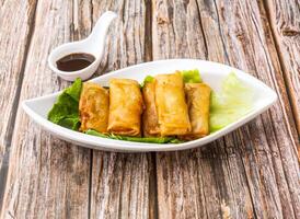 Vegetarian Spring Rolls with lettuce leaves and soy sauce served in dish isolated on wooden table side view of hong kong food photo