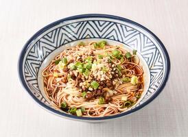 Sichuan Dan dan noodles topped with spring onion and nuts served in bowl isolated on white background side view of hong kong food photo