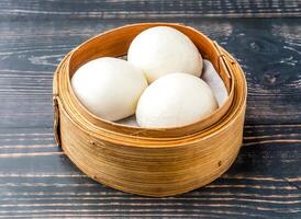 Steamed Quicksand Bun served in bamboo steamer isolated on wooden table side view of hong kong food photo