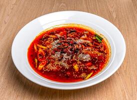 Sichuan Spicy boiled beef with red pepper, onion and sesame seeds served in bowl isolated on wooden table side view of hong kong food photo