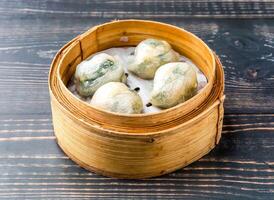 Steamed Shrimp and vegetable dumplings served in bamboo steamer isolated on wooden table side view of hong kong food photo