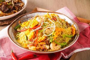 Xing zhou Fried Rice or Singapore Style Fried Rice including shrimp, vegetables, and egg served in pot isolated on napkin side view of hong kong food on wooden background photo