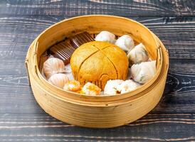 Dim Sum Platter including steamed buns, dumplings, and other savory delights served in bamboo steamer isolated on wooden table side view of hong kong food photo
