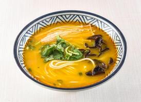 Golden Curry Noodle Soup topped with enoki mushrooms, wood ear mushrooms, and cilantro served in bowl isolated on white background side view of hong kong food photo