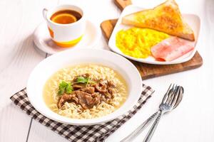 Beef Noodle Soup served on bowl alongside scrambled eggs, toast, and a cup of lime green tea isolated white table side view of hong kong breakfast morning meal photo