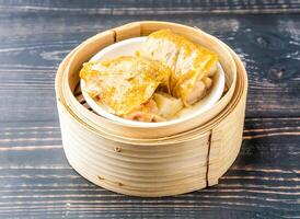 Steamed Chicken Feet with Mushroom wrapped in bean curd sheet served in bamboo steamer isolated on wooden table side view of hong kong food photo