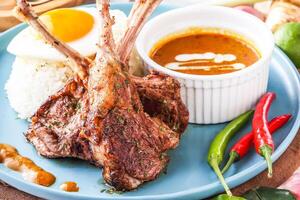 Pan fried Lamb Rack or lamb chops with with curry, rice and sunny side up egg served in plate with chili peppers isolated on napkin closeup side view of hong kong food photo