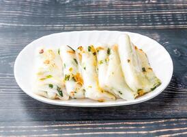 Pan fried rice rolls with scallops served in tray dish isolated on wooden table side view of hong kong food photo