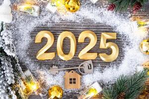 New Year 2025 golden numbers and House key with tiny form of home on festive grey wooden background flatlay, lights of garlands, greeting card. Housing, real estate, relocation, mortgage, insurance photo