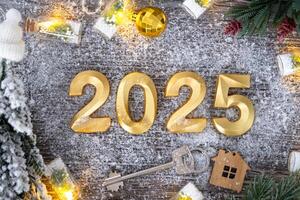 New Year 2025 golden numbers and House key with tiny form of home on festive grey wooden background flatlay, lights of garlands, greeting card. Housing, real estate, relocation, mortgage, insurance photo