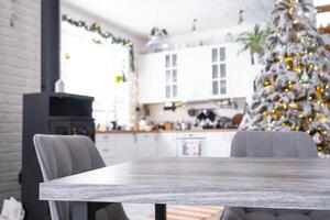 Grey Wooden empty table to demonstrate product with space for text with upholstered chairs in white kitchen, modern interior with Christmas tree and fairy lights. New Year, Christmas mood, cozy home. photo