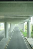 A long, straight road passing through a concrete overpass structure with multiple arched openings, surrounded by green foliage at new yogyakarta international airport photo