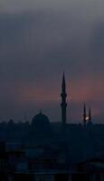 A silhouette of a Middle Eastern city skyline with intricate domed buildings and slender minarets against a foggy, gray background at dusk, with hints of orange and purple peeking through the fog 1 photo