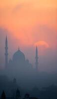 A silhouette of a Middle Eastern city skyline with detailed domed buildings and elegant minarets against a dense foggy, gray background during sunset, with vibrant colors merging into the fog photo