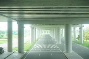 A long, straight road passing through a concrete overpass structure with multiple arched openings, surrounded by green foliage at new yogyakarta international airport photo