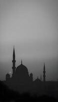 A silhouette of a Middle Eastern city skyline with intricate domed buildings and slender minarets against a foggy, gray background at dusk, with hints of orange and purple peeking through the fog 2 photo