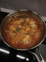 Aromatic tomato sauce cooking in a pan, topped with grated cheese and herbs, creating a flavorful and comforting dish photo