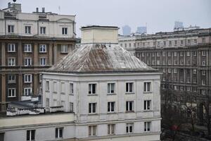 Weathered roof stands out against a backdrop of grey buildings at Muranowska street in Warsaw Poland. The overcast sky hints at approaching rain, creating a moody atmosphere in the cityscape. photo