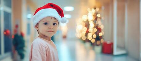 Young child wearing a santa claus hat in a hospital corridor with a blurred christmas tree in the background photo