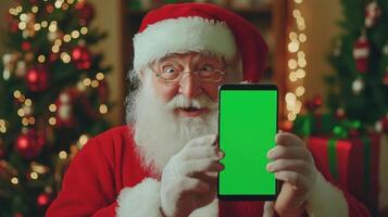 Santa claus pointing at smartphone with green chroma key screen near decorated christmas tree photo