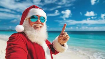 Santa claus wearing sunglasses pointing finger up enjoying summer holidays on tropical sandy beach photo