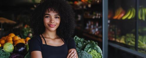 Confident young greengrocer posing with arms crossed in her grocery store photo