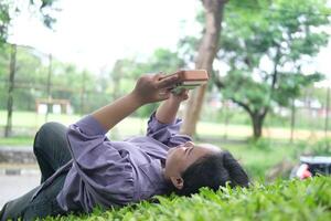Asian woman plays a kalimba in a green park on a sunny day. The calm melodies and lush leaves create a peaceful and relaxing scene photo