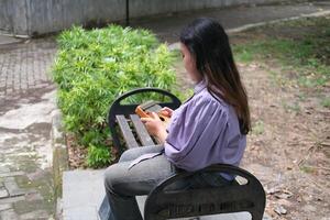 young Asian woman plays a kalimba while relaxing in a green city park during summer. The bright sunlight, lush surroundings, and soft melodies create a calm and refreshing outdoor scene photo
