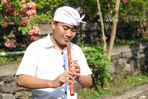 Portrait of Balinese Asian man playing traditional bamboo flute in outdoor park photo