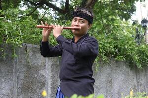 Portrait of Balinese man playing traditional bamboo flute at park in the morning photo