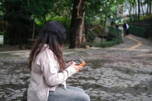 Asian woman plays a kalimba in a green park on a sunny day. The calm melodies and lush leaves create a peaceful and relaxing scene photo