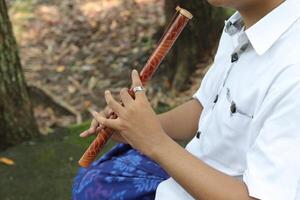 Close up of male hand playing traditional bamboo flute against city park background photo