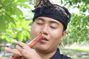 Portrait of Balinese man playing traditional bamboo flute at park in the morning photo