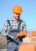 Male construction worker in uniform and helmet on construction of red brick house photo
