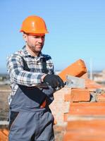 Bricklayer industrial worker installing brick masonry on exterior wall with trowel putty knife photo