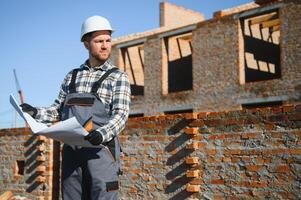 An architect or engineer on the construction of brick houses holds the construction plan in his hands and checks the execution of the work photo
