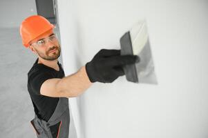 man drywall worker or plasterer putting mesh tape for plasterboard on a wall using a spatula and plaster. photo