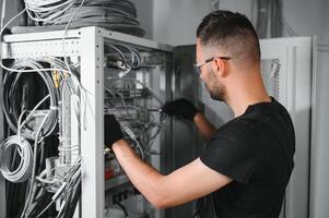 A technician works with server equipment in a data center. A man commutes wires in a server room photo