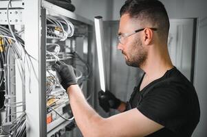 A technician works with server equipment in a data center. A man commutes wires in a server room photo