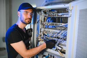 A technician works with server equipment in a data center. A man commutes wires in a server room photo