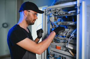 A technician works with server equipment in a data center. A man commutes wires in a server room photo