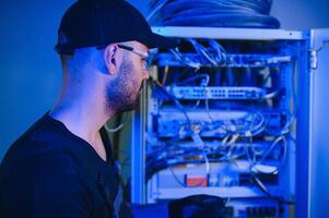 A technician works with server equipment in a data center. A man commutes wires in a server room photo