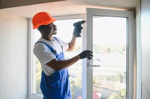 Workman in overalls installing or adjusting plastic windows in the living room at home photo