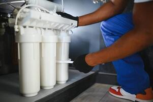 Plumber installs or change water filter. Replacement aqua filter. Repairman installing water filter cartridges in a kitchen photo