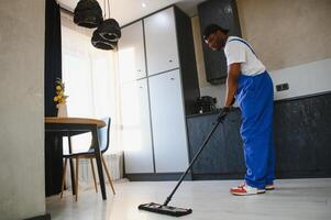 Man janitor with mop in hands from cleaning service washing gray floor in uniform. photo